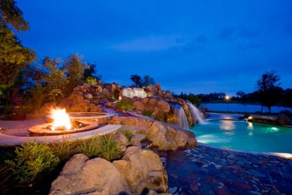outdoor propane fire pit next to pool with waterfall